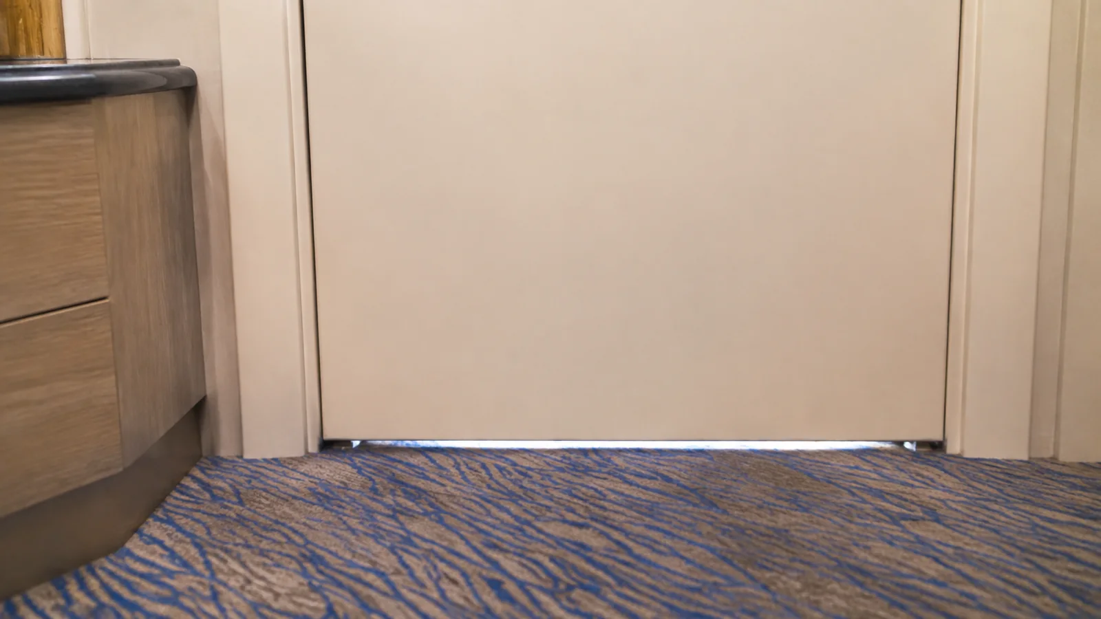 Gap beneath a closed cabin door above patterned carpeting.