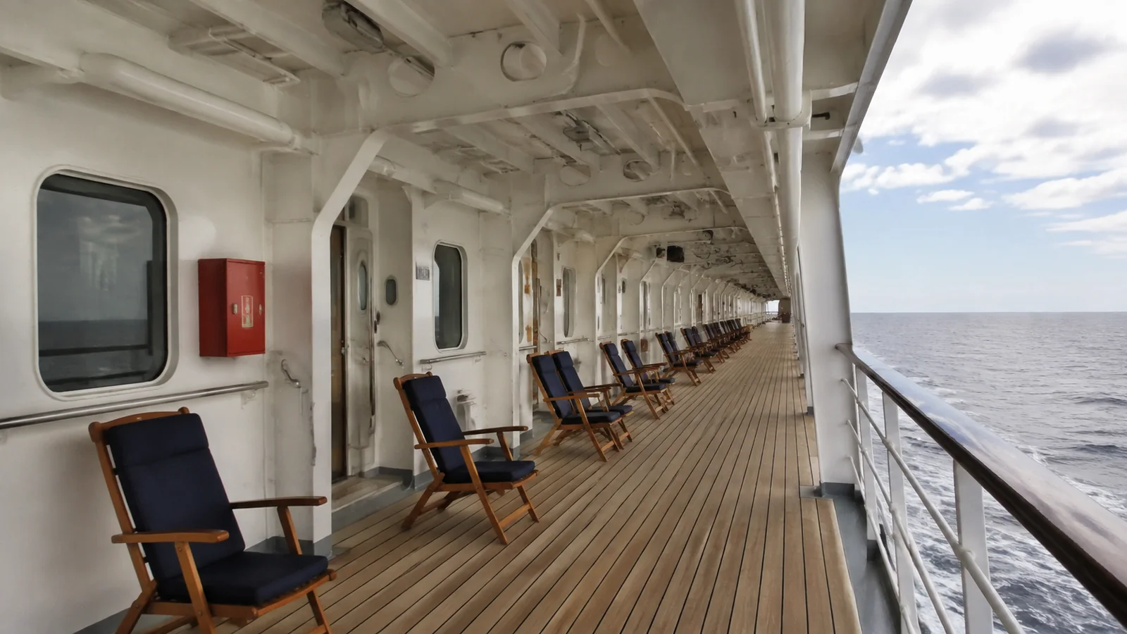 Wooden deck chairs line a covered promenade beside the sea.