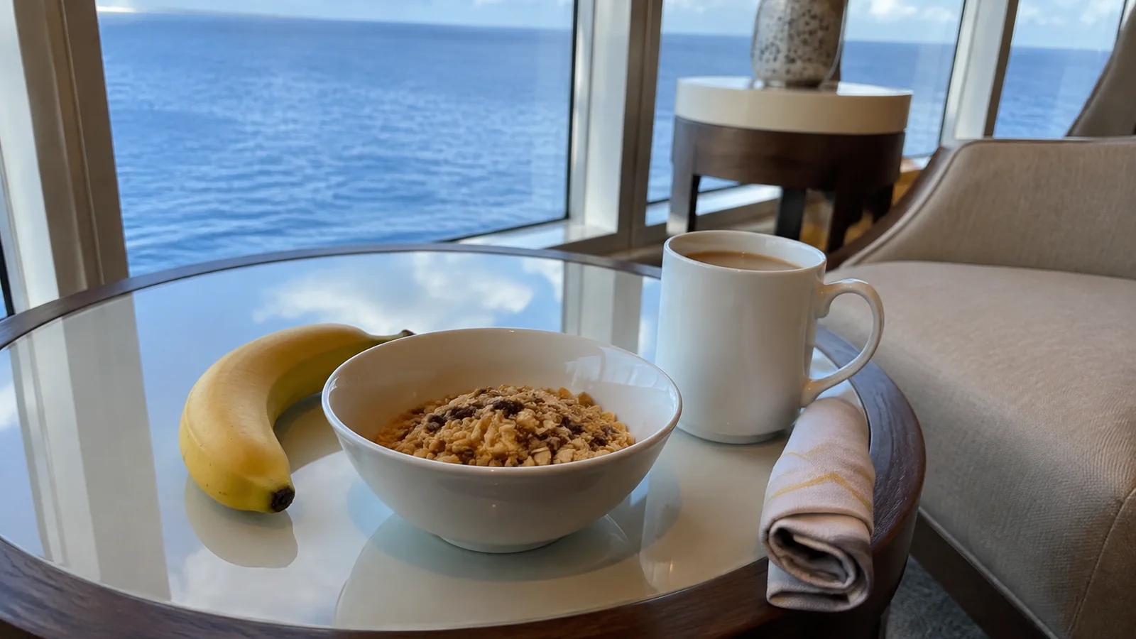 Cereal bowl, banana and coffee sit on a table overlooking the sea.