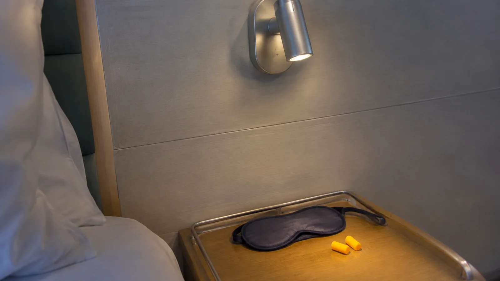 Sleep mask and earplugs rest below a bedside reading lamp.