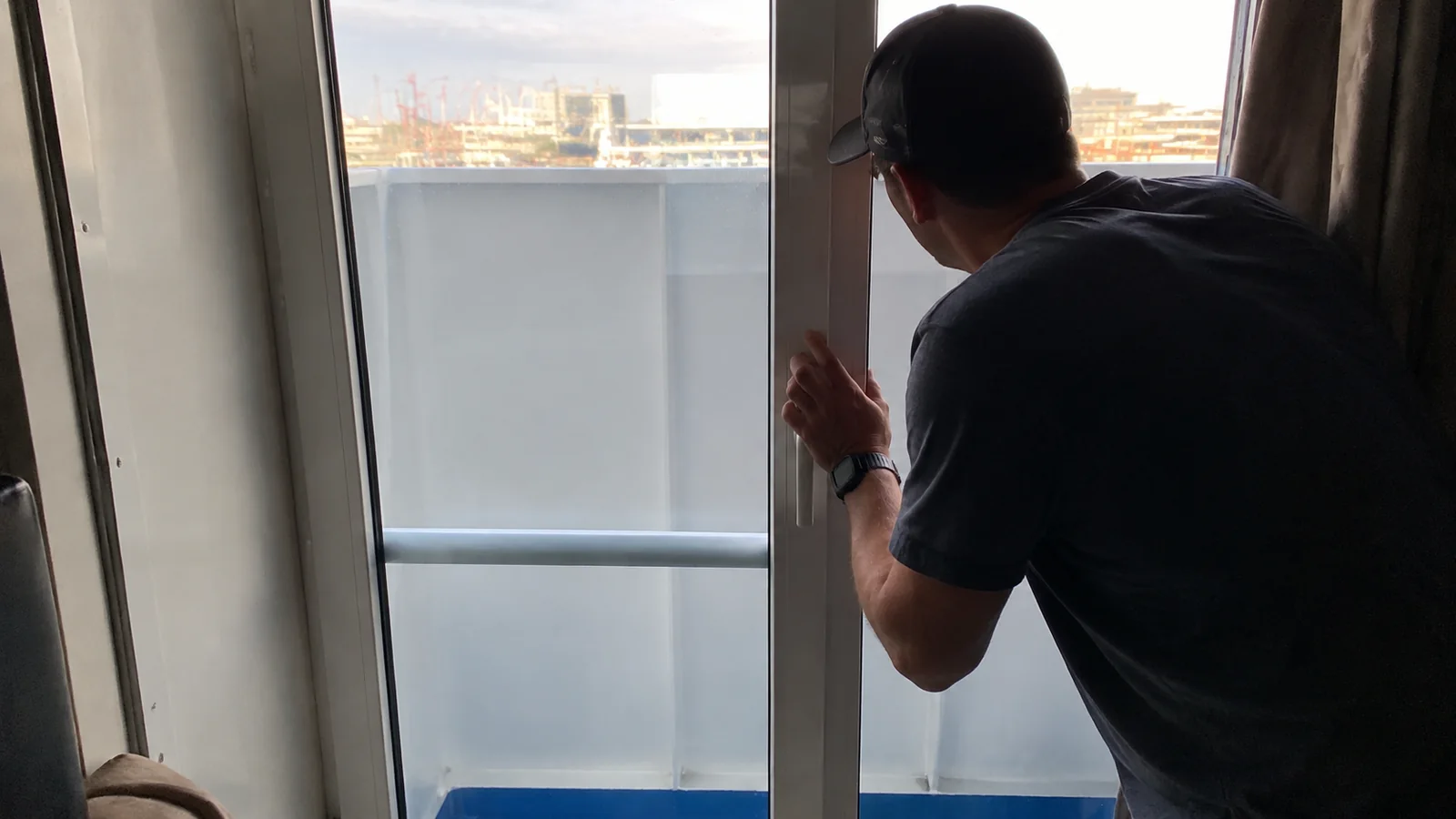 Man looking around a balcony partition toward a cruise port