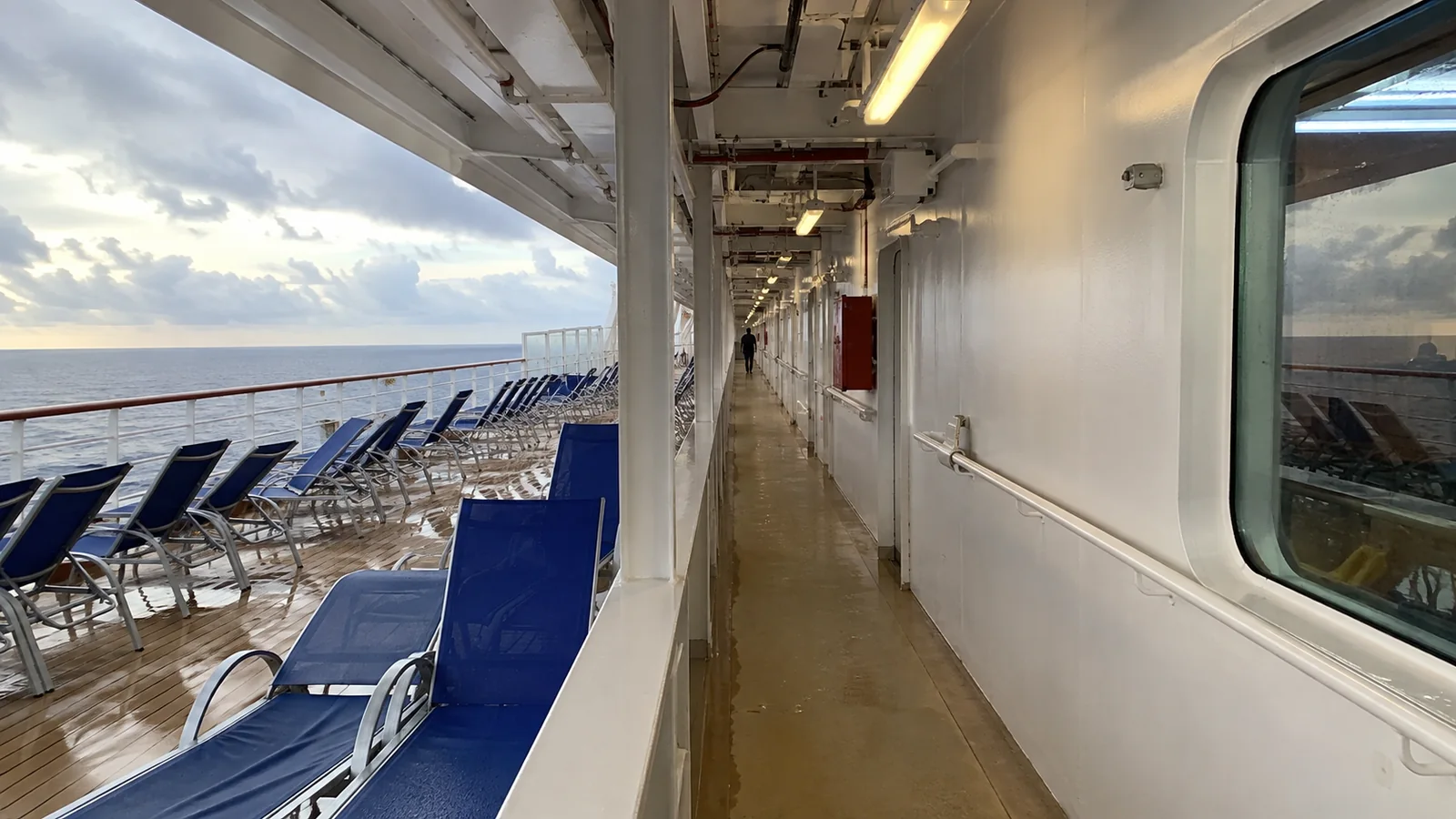 Covered cruise ship promenade with blue lounge chairs overlooking the ocean