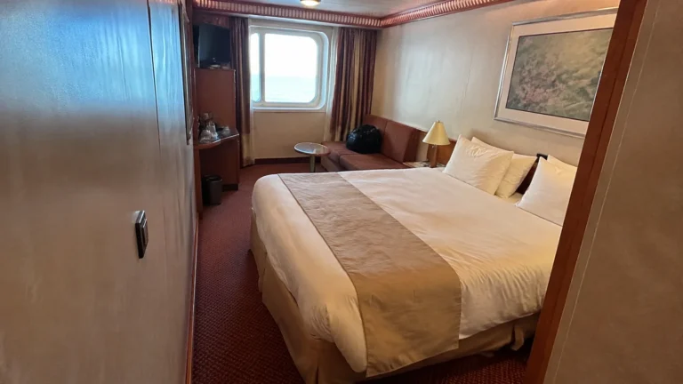 Cruise cabin with a double bed and seating area beside a window