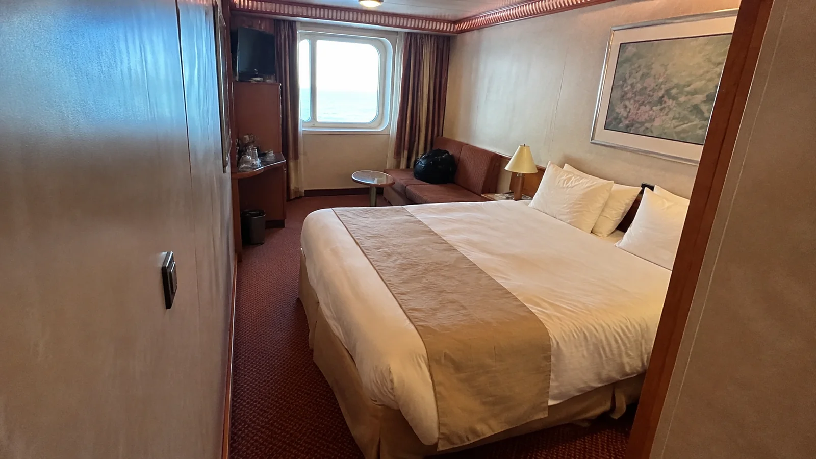 Cruise cabin with a double bed and seating area beside a window