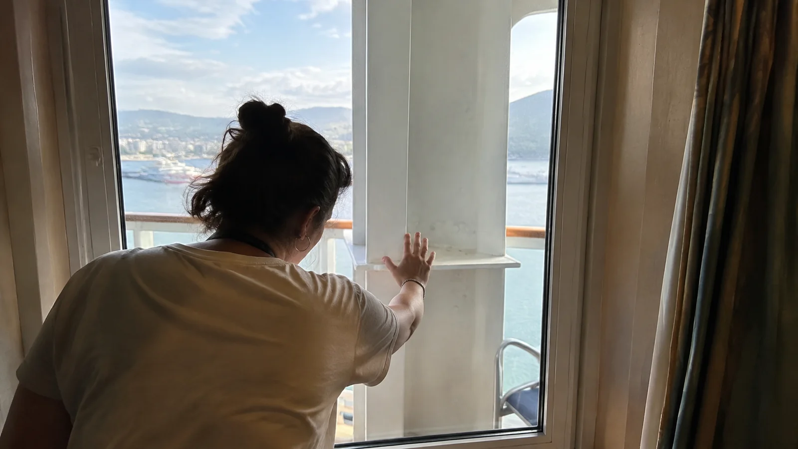 Woman looking past a wide support outside a cruise cabin balcony