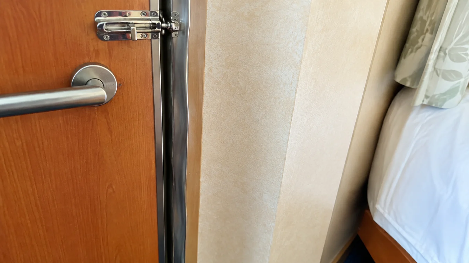 Close-up of a latched connecting door beside a cruise cabin bed