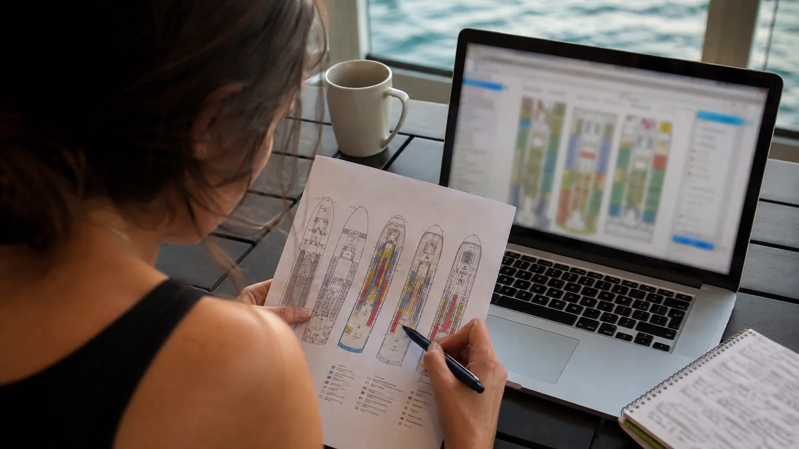 Woman marking a printed cruise ship deck plan beside a laptop