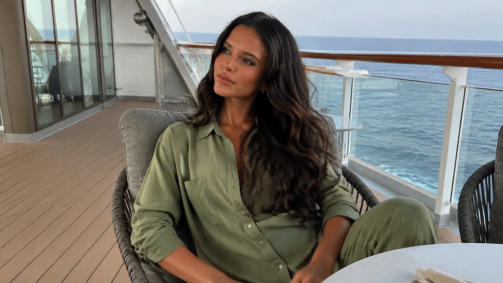 Woman sits in a wicker chair beside a glass ship railing.