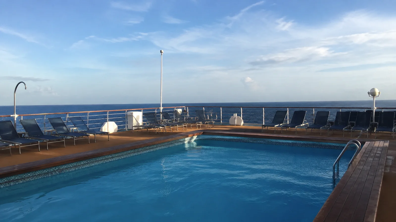 Empty outdoor pool and lounge chairs overlook the open sea.