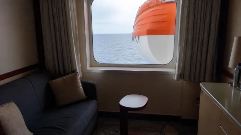 Orange and white lifeboat partially blocks a stateroom window view.