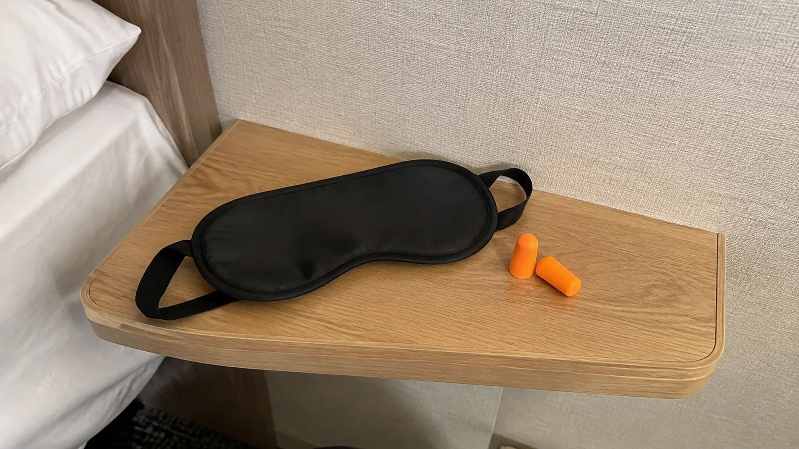 Black sleep mask and orange earplugs rest on a bedside table.