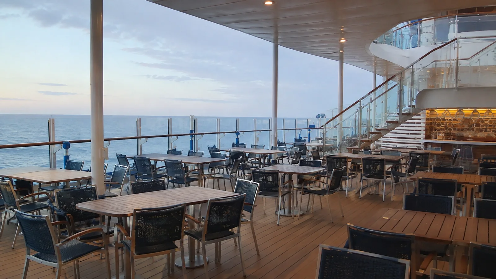 Empty outdoor dining tables overlook the sea beneath a ship overhang.