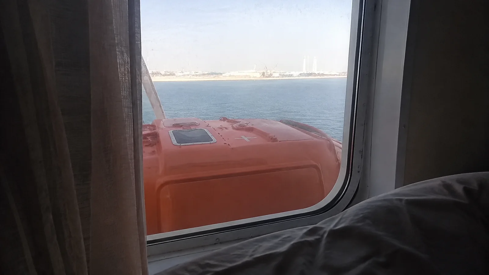 Orange lifeboat partly blocking the view through a cabin window.