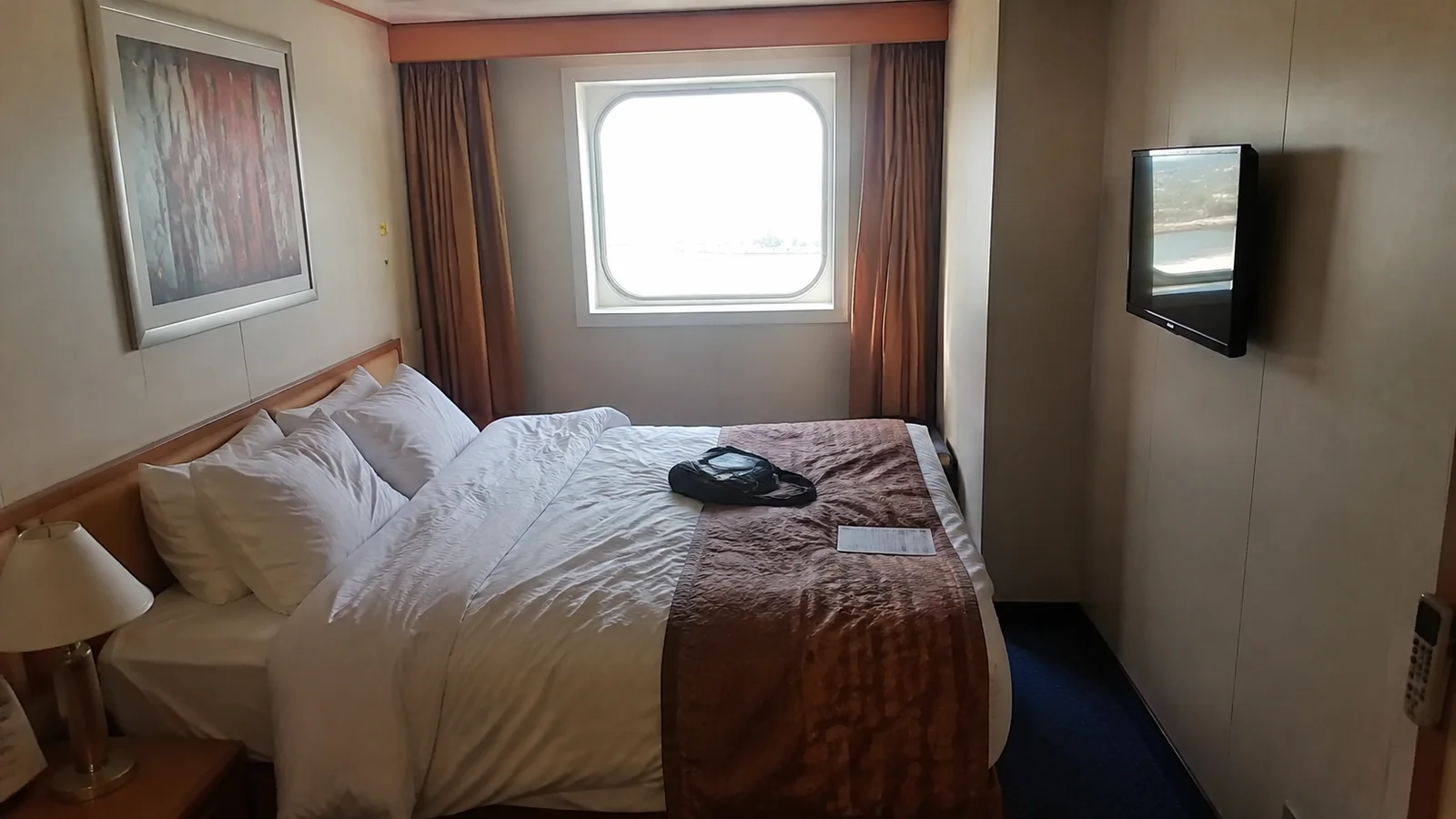 Cruise cabin with a double bed, wall-mounted television, and window