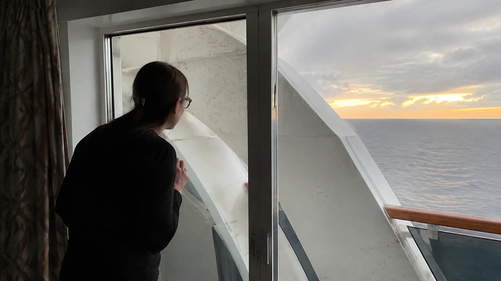 Woman looking past a ship support toward the ocean at sunset