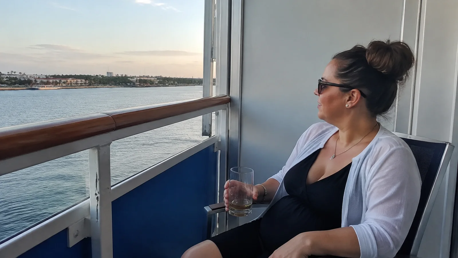 Woman holding a glass relaxes on a balcony overlooking the water.