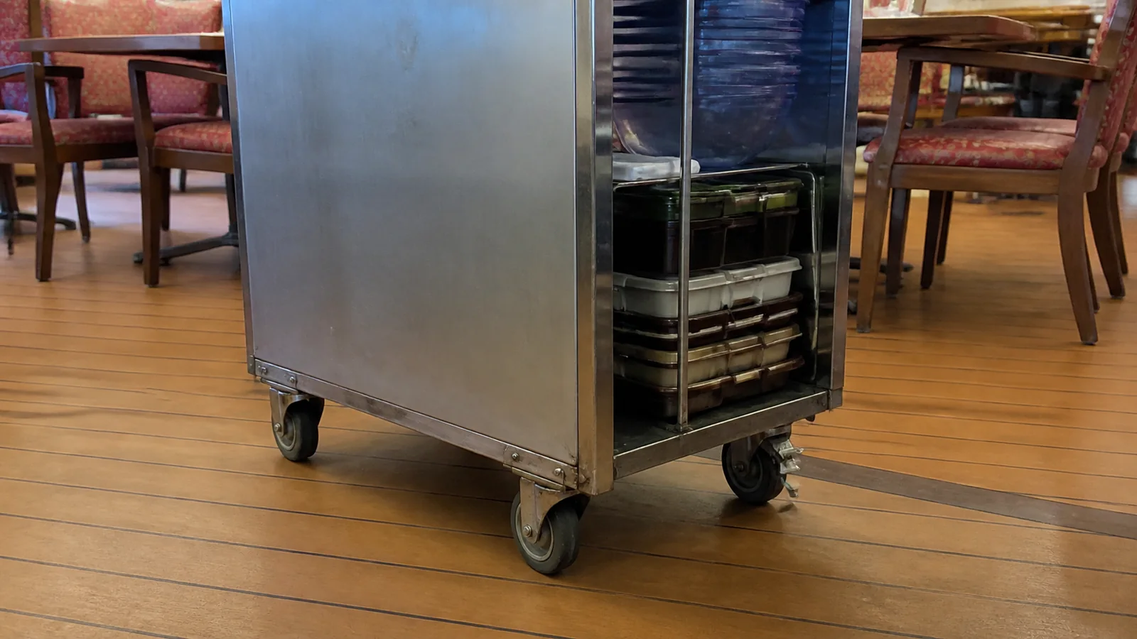 Metal service cart stands between dining tables on a wooden floor.