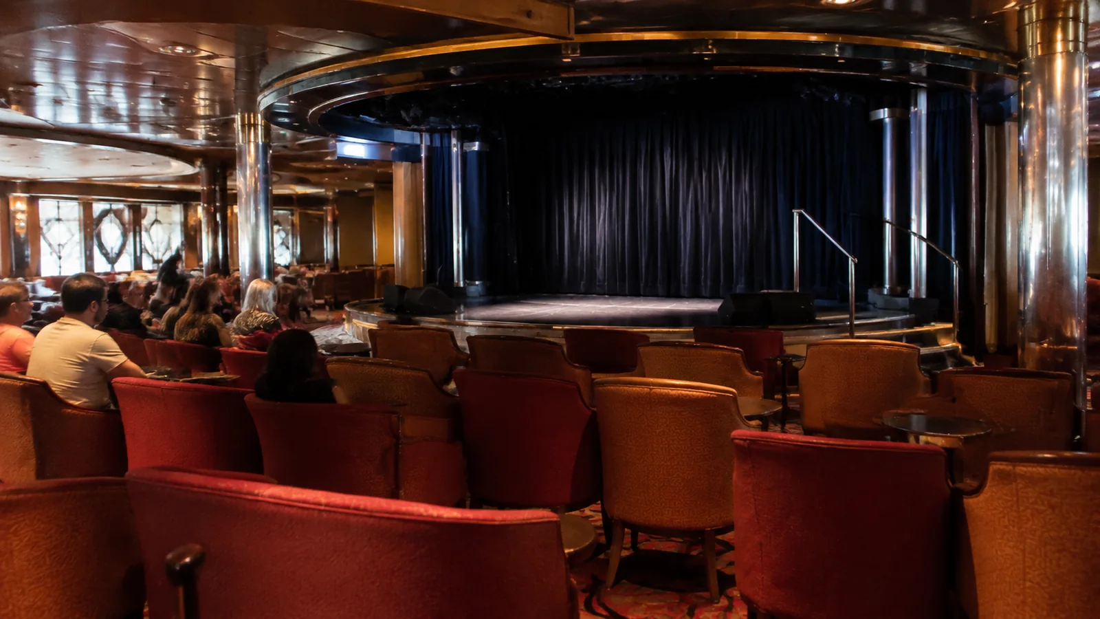 Passengers sit before a curtained stage in a theater.