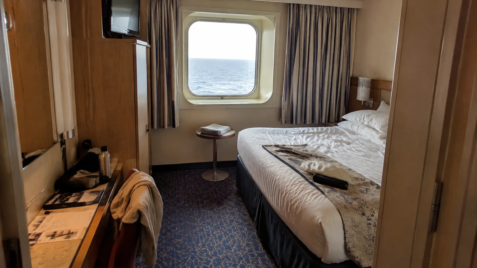 Cruise cabin with a bed, desk, and ocean-view window