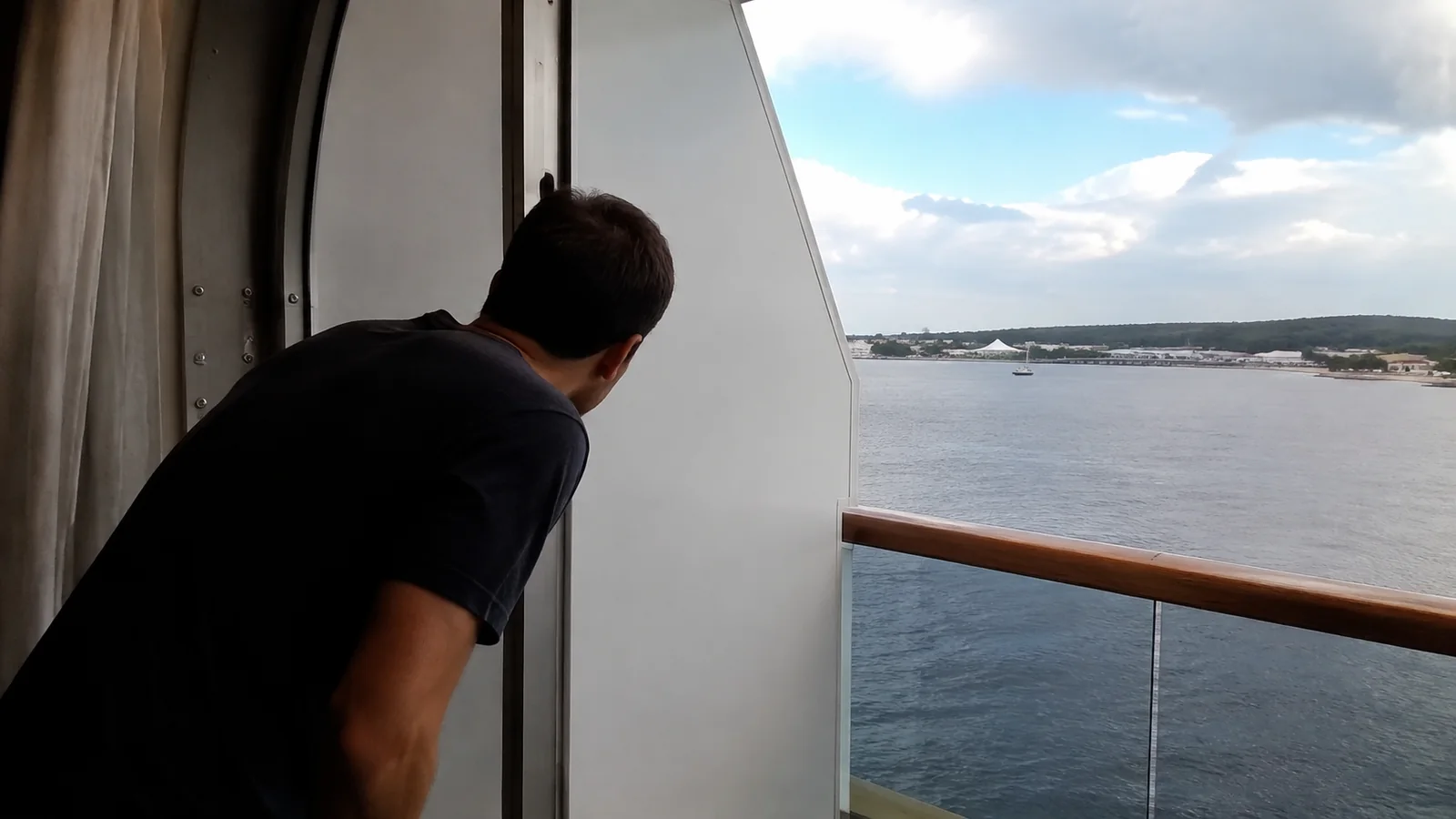 Man looking past a balcony partition toward the coastline