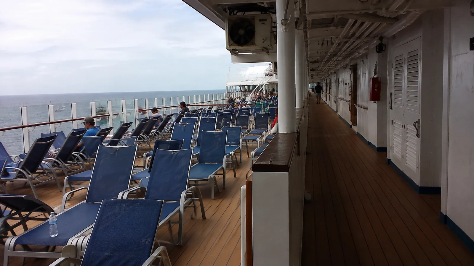 Passengers relaxing on blue lounge chairs along a cruise ship promenade
