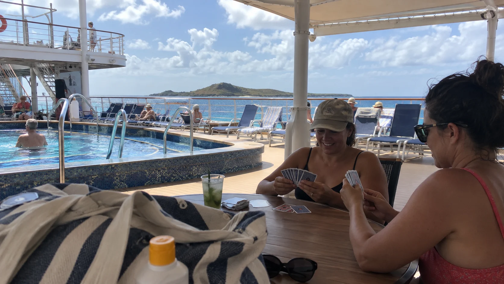 Friends playing cards beside an uncrowded pool on a smaller cruise ship.