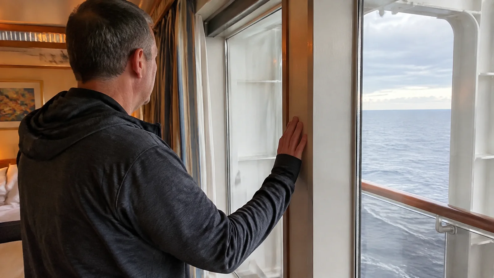 Man looking out from a cruise cabin balcony doorway toward the ocean