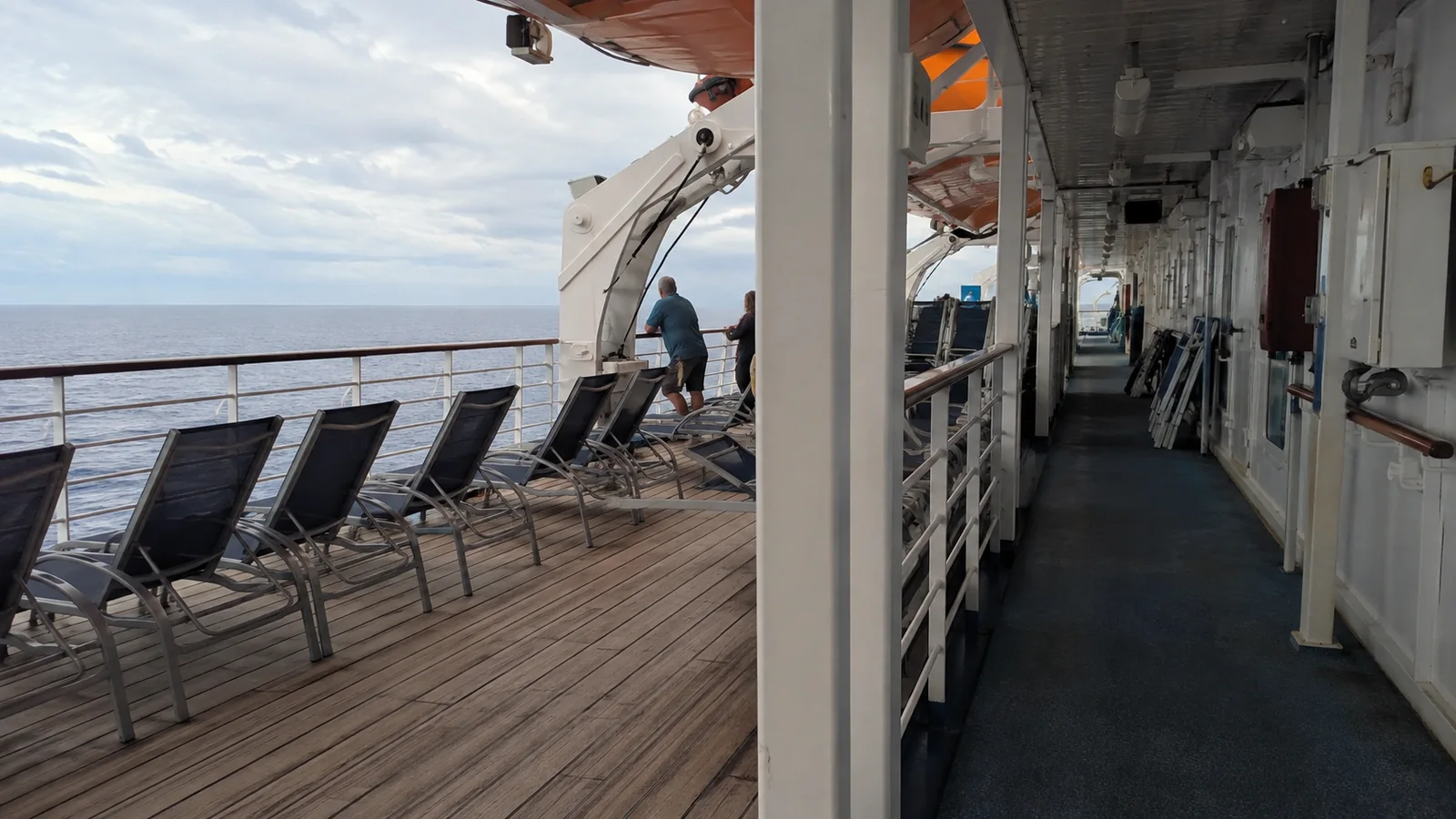Cruise ship promenade with lounge chairs and a covered walkway