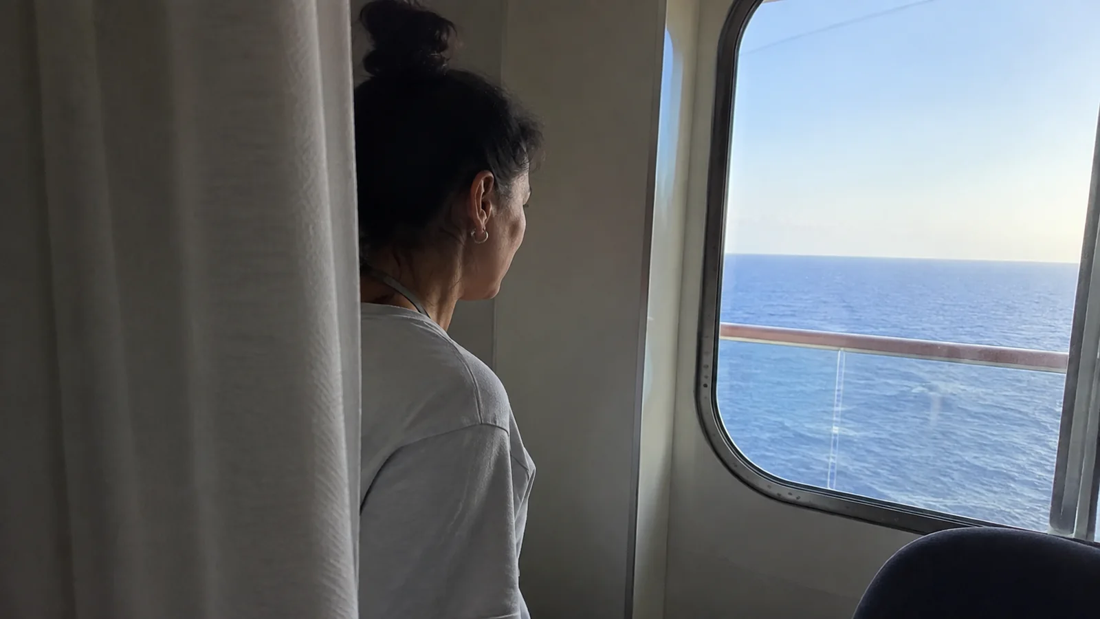 Woman looks through a cabin window toward the sea.