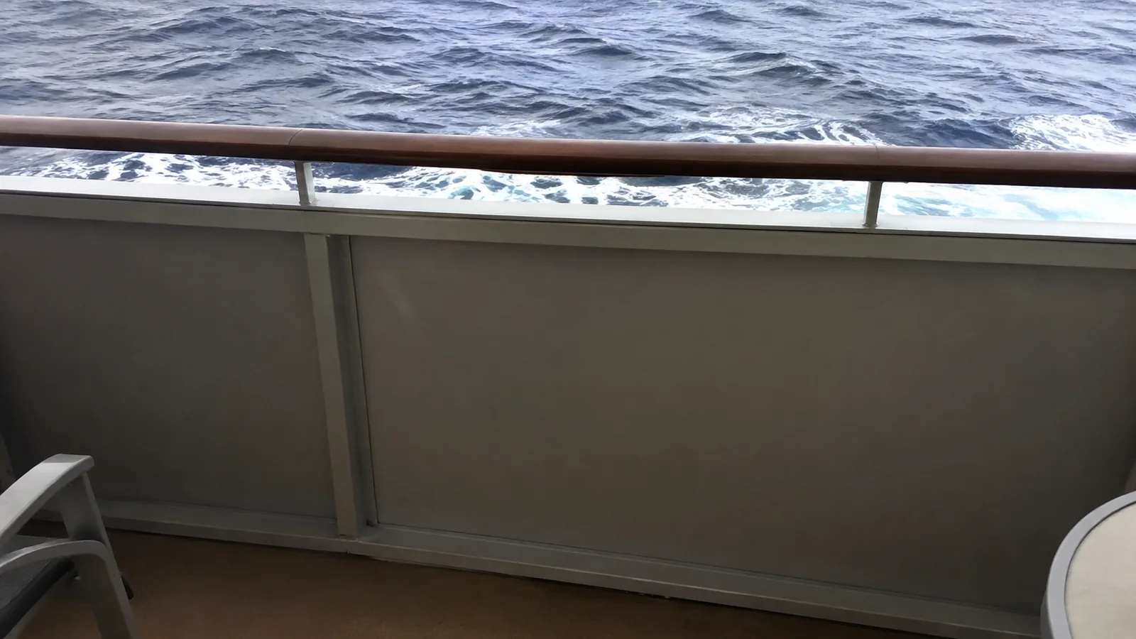 Solid balcony panel beneath a railing partially obscures the ocean view.