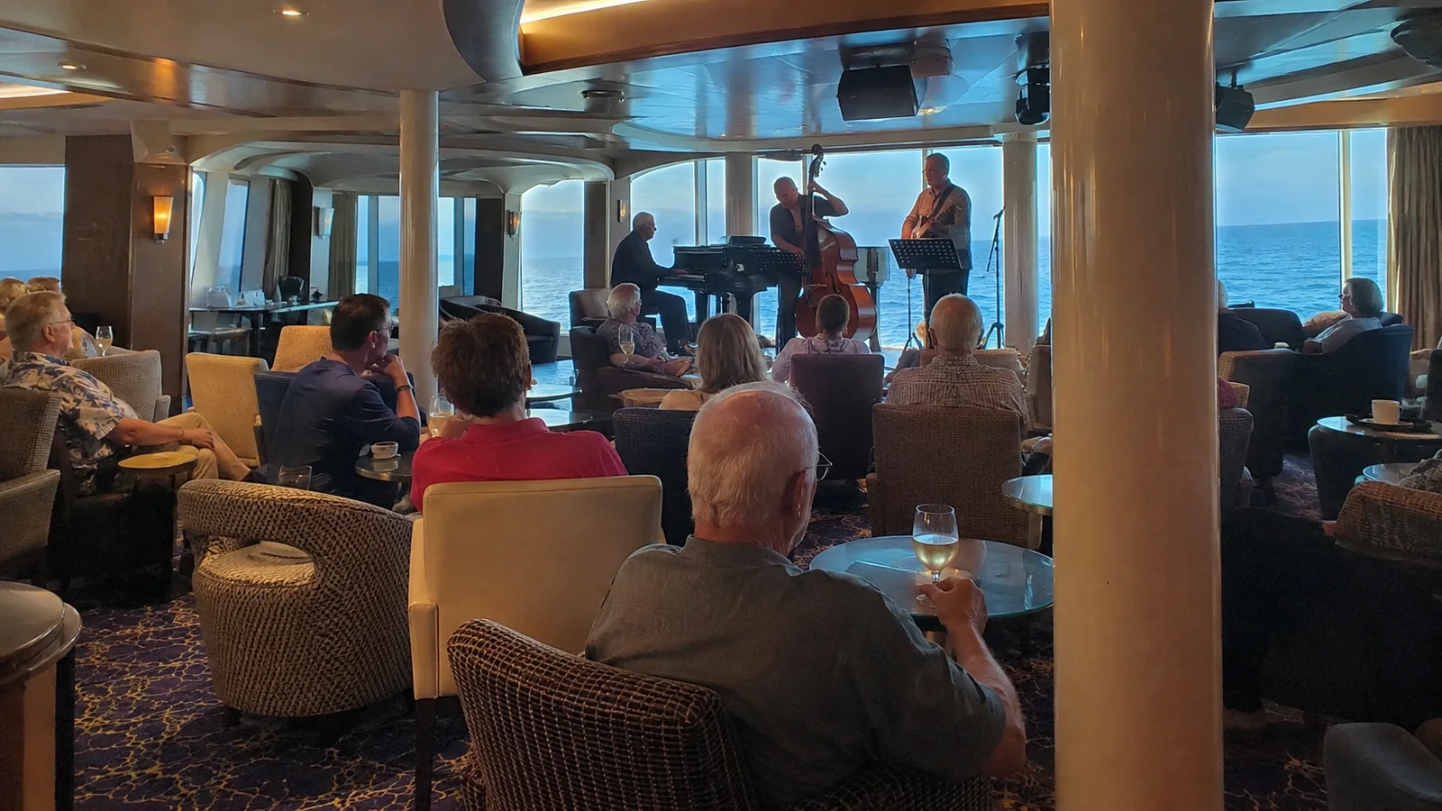 Passengers watch musicians perform in a lounge overlooking the ocean.