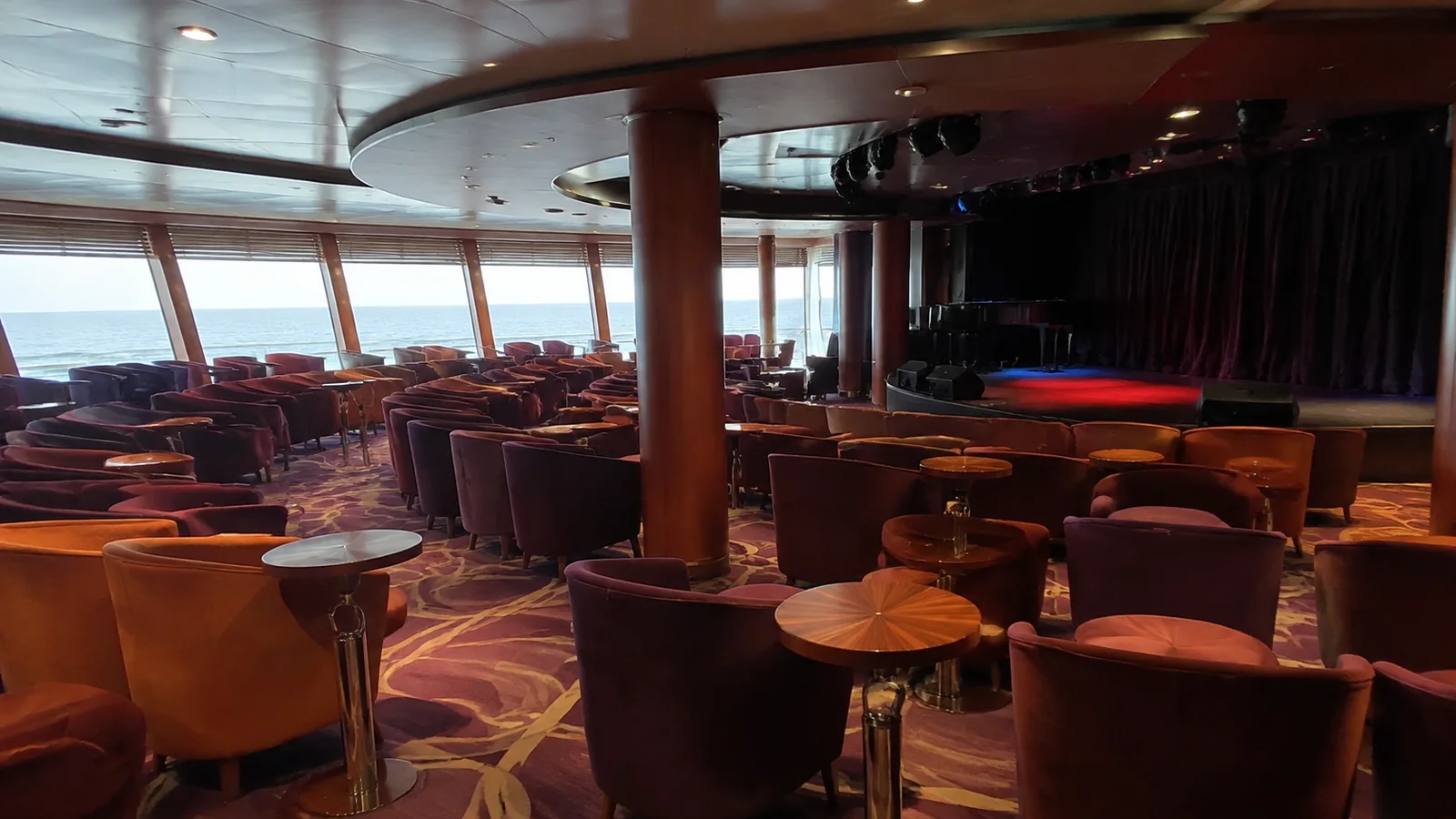 Ship lounge with rows of armchairs facing a small stage.