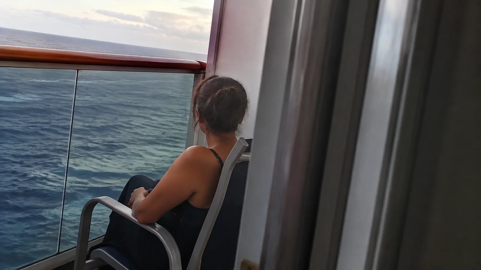 Woman sits on a balcony chair looking over the ocean.