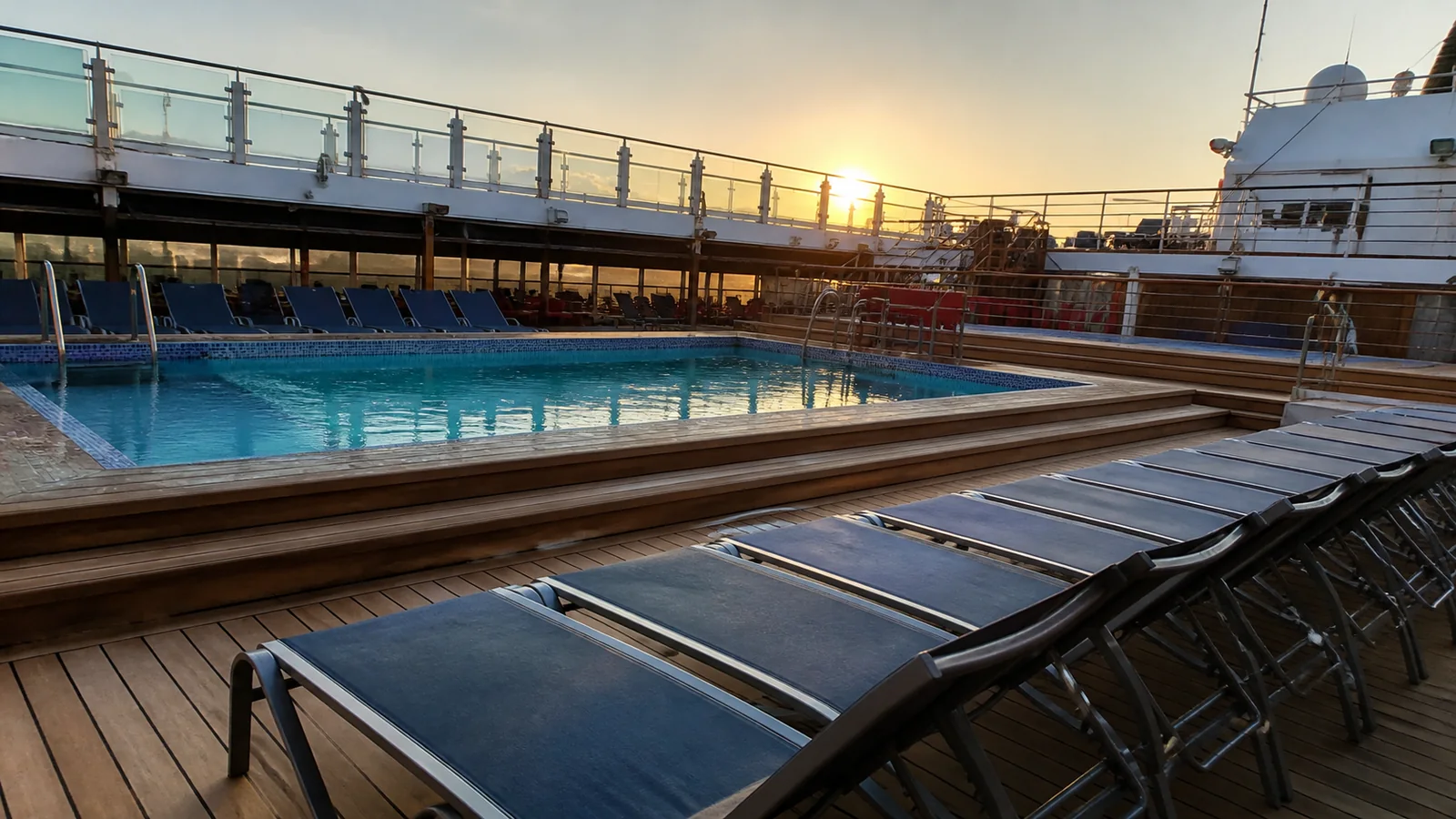 Empty lounge chairs surround a ship pool in warm evening light.