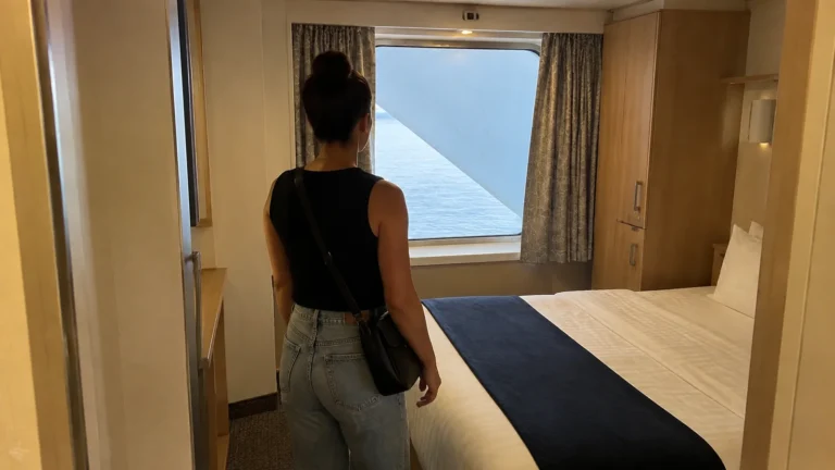Woman enters a cabin with a bed beside a window.