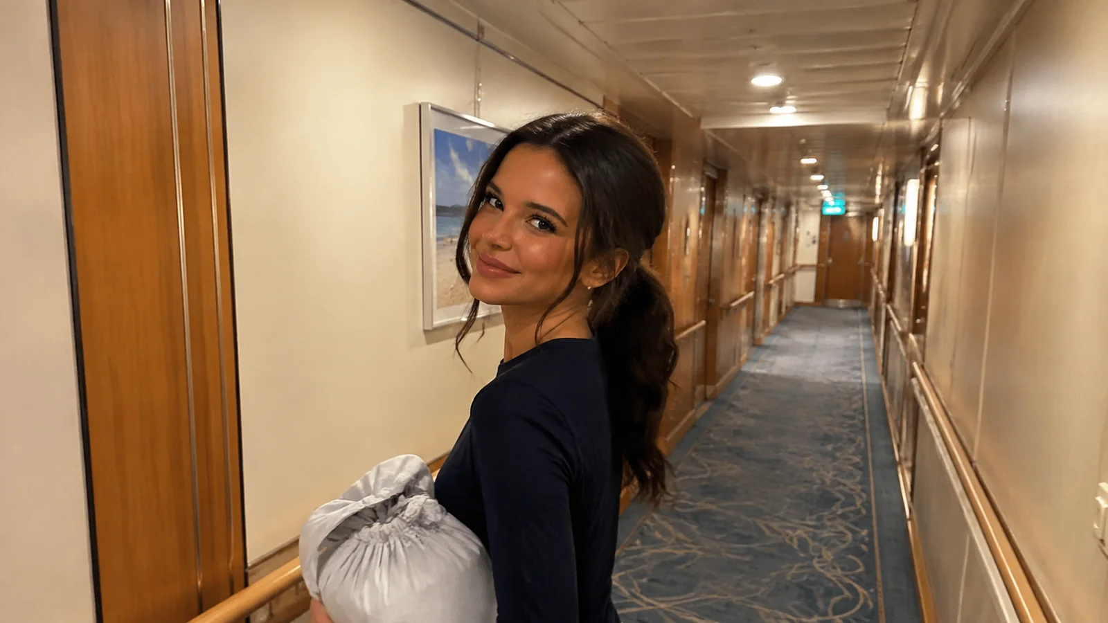 Woman carrying clothing looks back in a long cabin corridor.