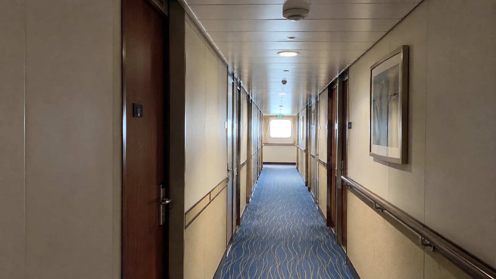 Narrow blue-carpeted hallway lined with cabin doors.