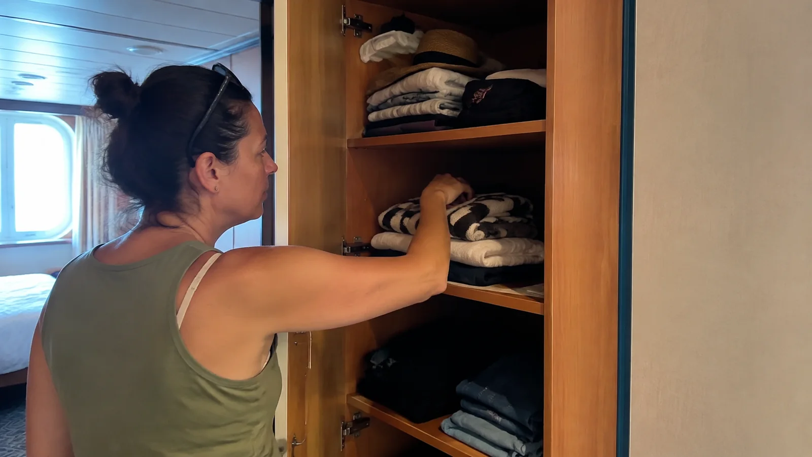 Passenger organizing folded clothing on wardrobe shelves.