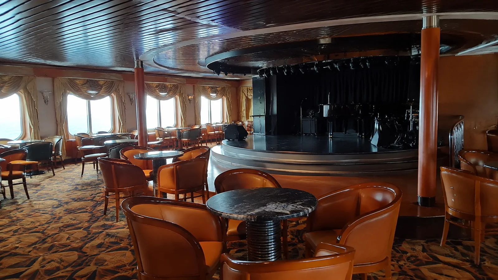 Empty ship lounge has round tables and a dark stage.