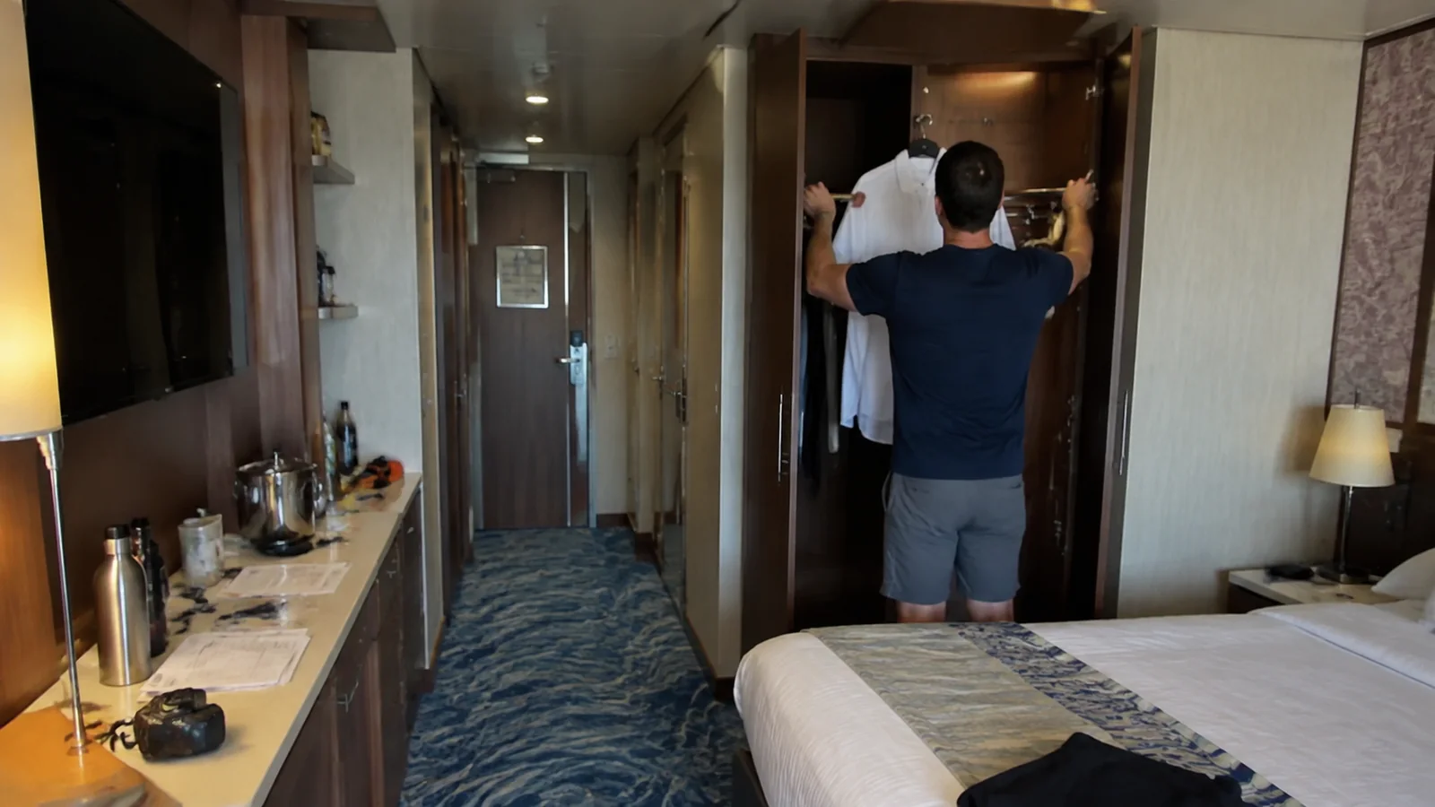 Man hangs a white shirt inside a stateroom wardrobe.