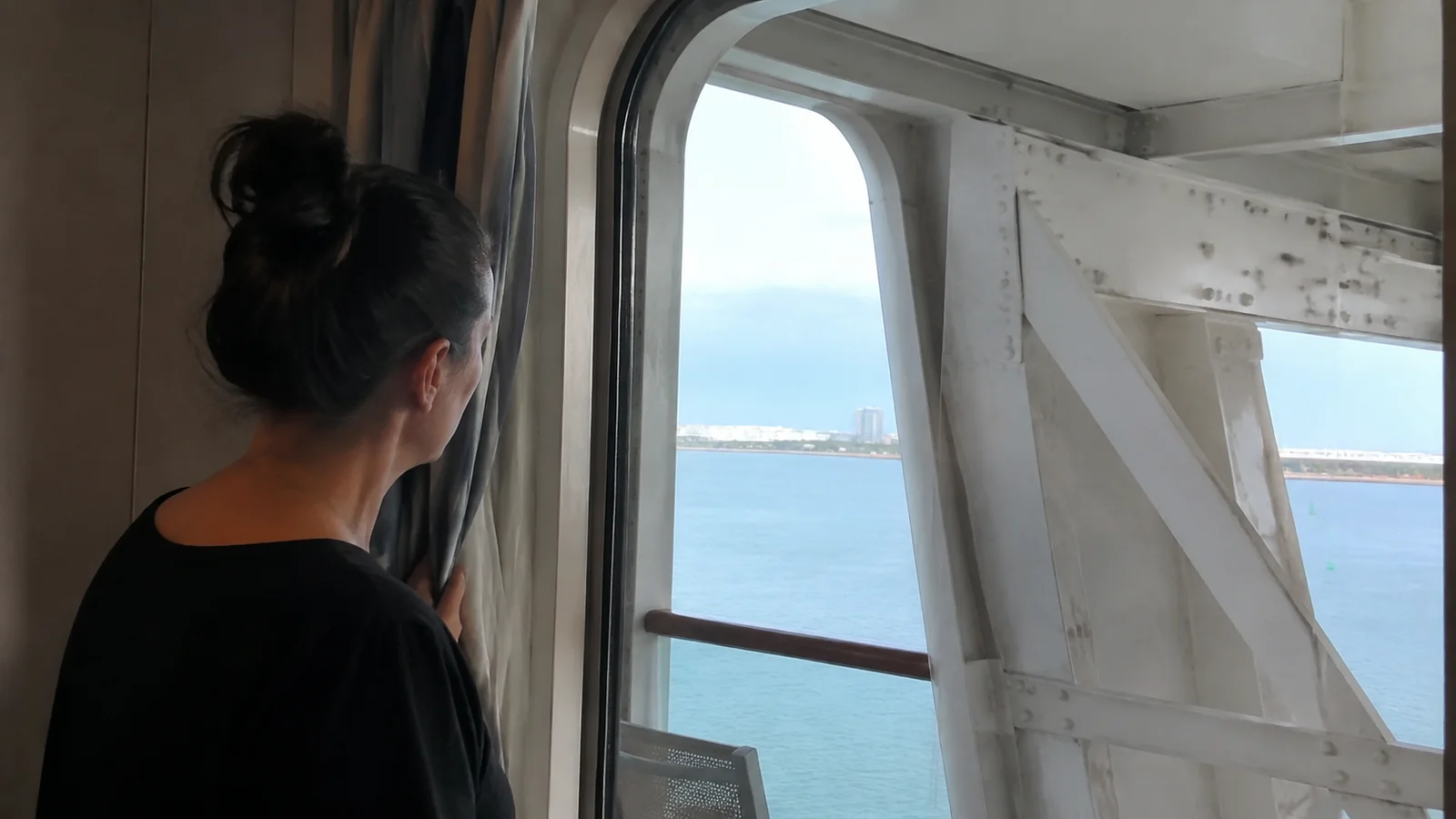 Woman looking through a cruise cabin window with a partially obstructed sea view