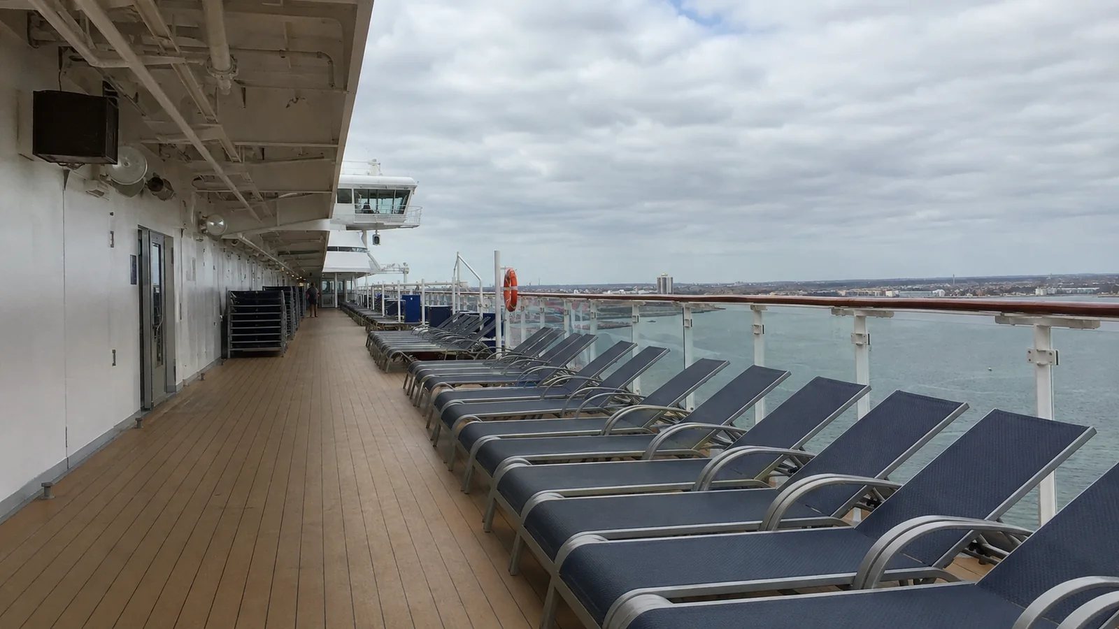 Empty lounge chairs along a covered cruise ship promenade in port