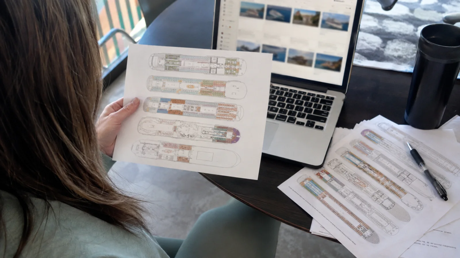 Woman comparing printed cruise ship deck plans beside a laptop