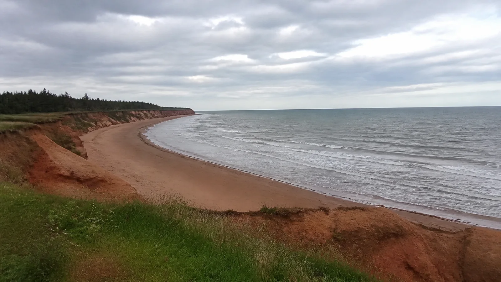 Reddish cliffs curve around a quiet sandy shoreline.