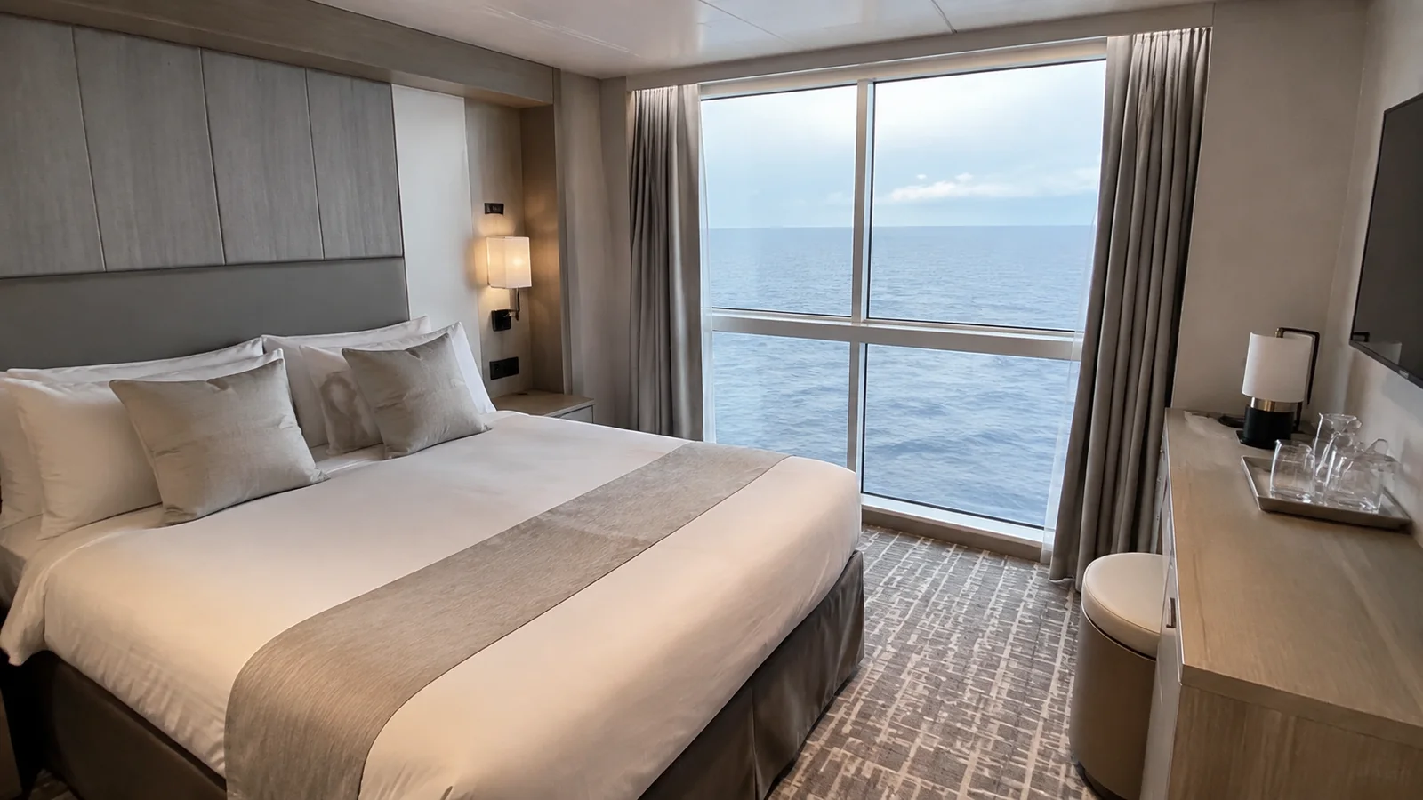Modern stateroom contains a double bed and tall ocean window.