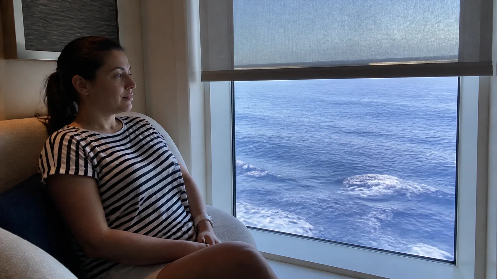 Woman sits beside a large window overlooking the open ocean.
