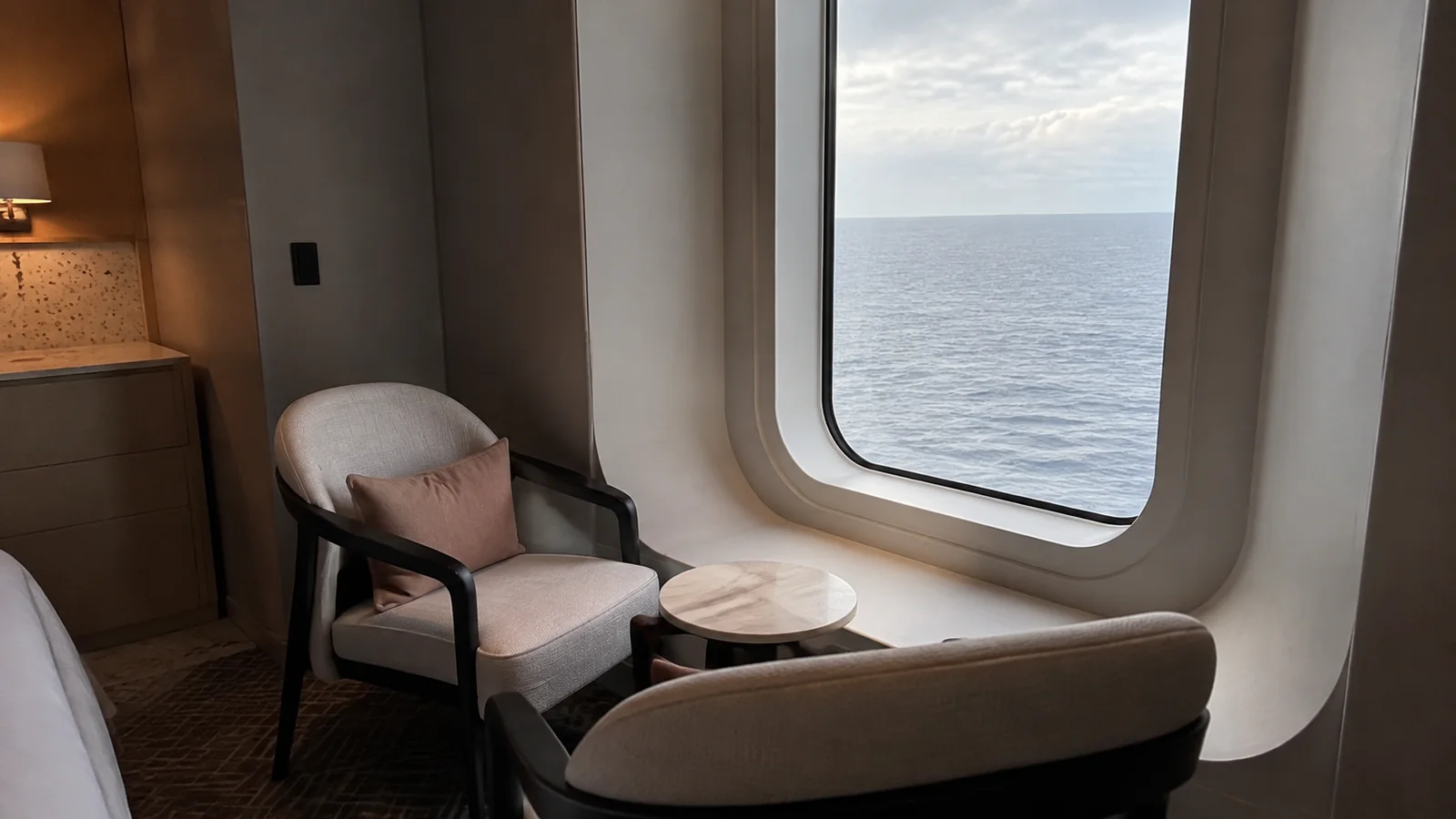 Two chairs and a small table sit beside a ship window.
