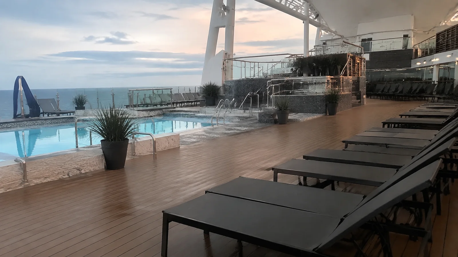 Empty lounge chairs face a ship pool and open deck.