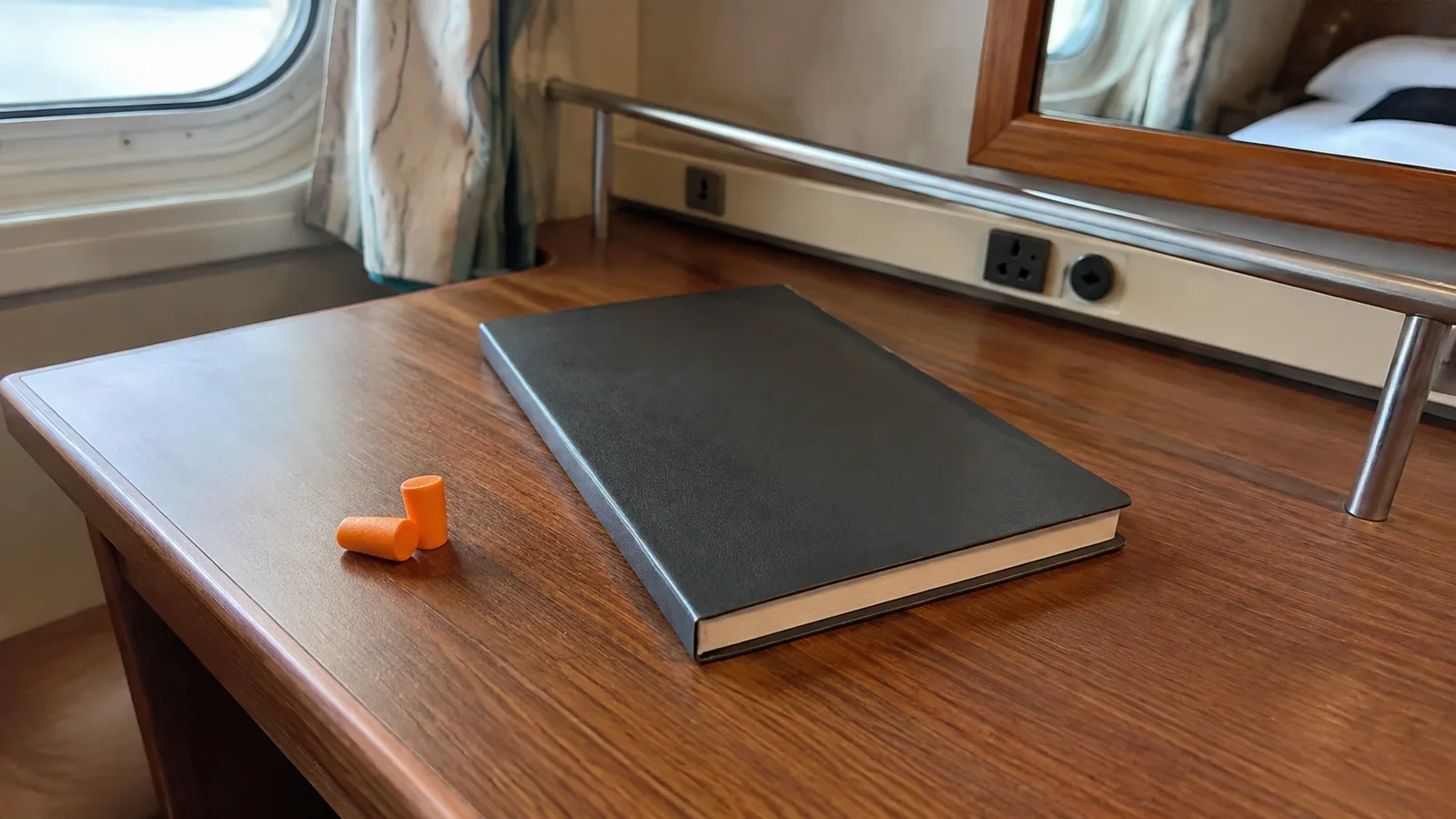Orange earplugs and a dark notebook lie on a stateroom desk.