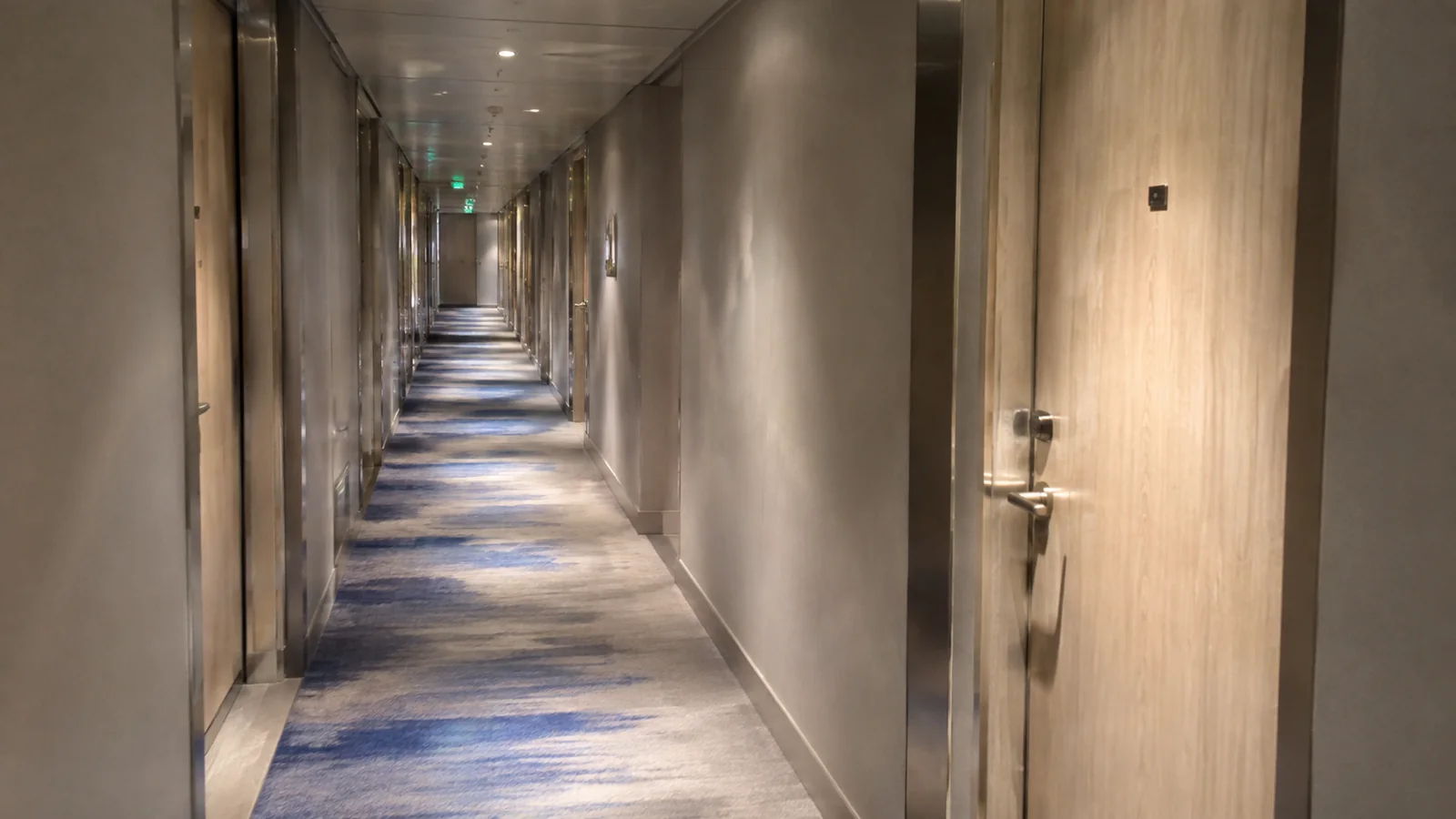 Long empty stateroom corridor is lined with pale wooden doors.